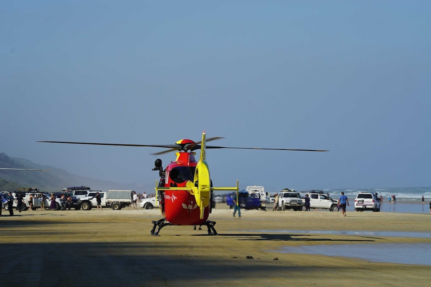 A helicopter sitting on a beach with multiple vehicles in the background.