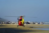 A helicopter sitting on a beach with multiple vehicles in the background.