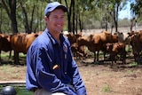 Farmer Stuart Barrett sits on a water trough in front of cattle.