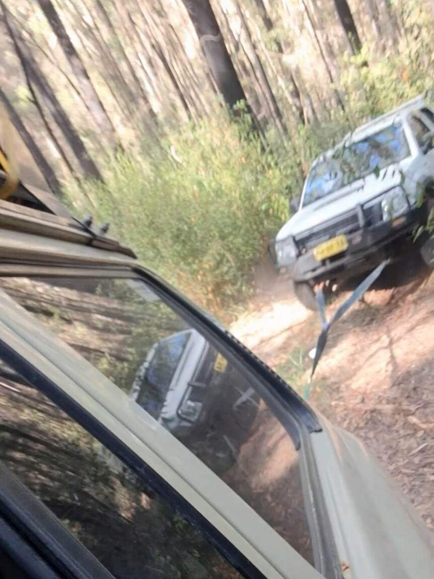 A 4WD towing another 4WD up a steep bush road with a cable between them.