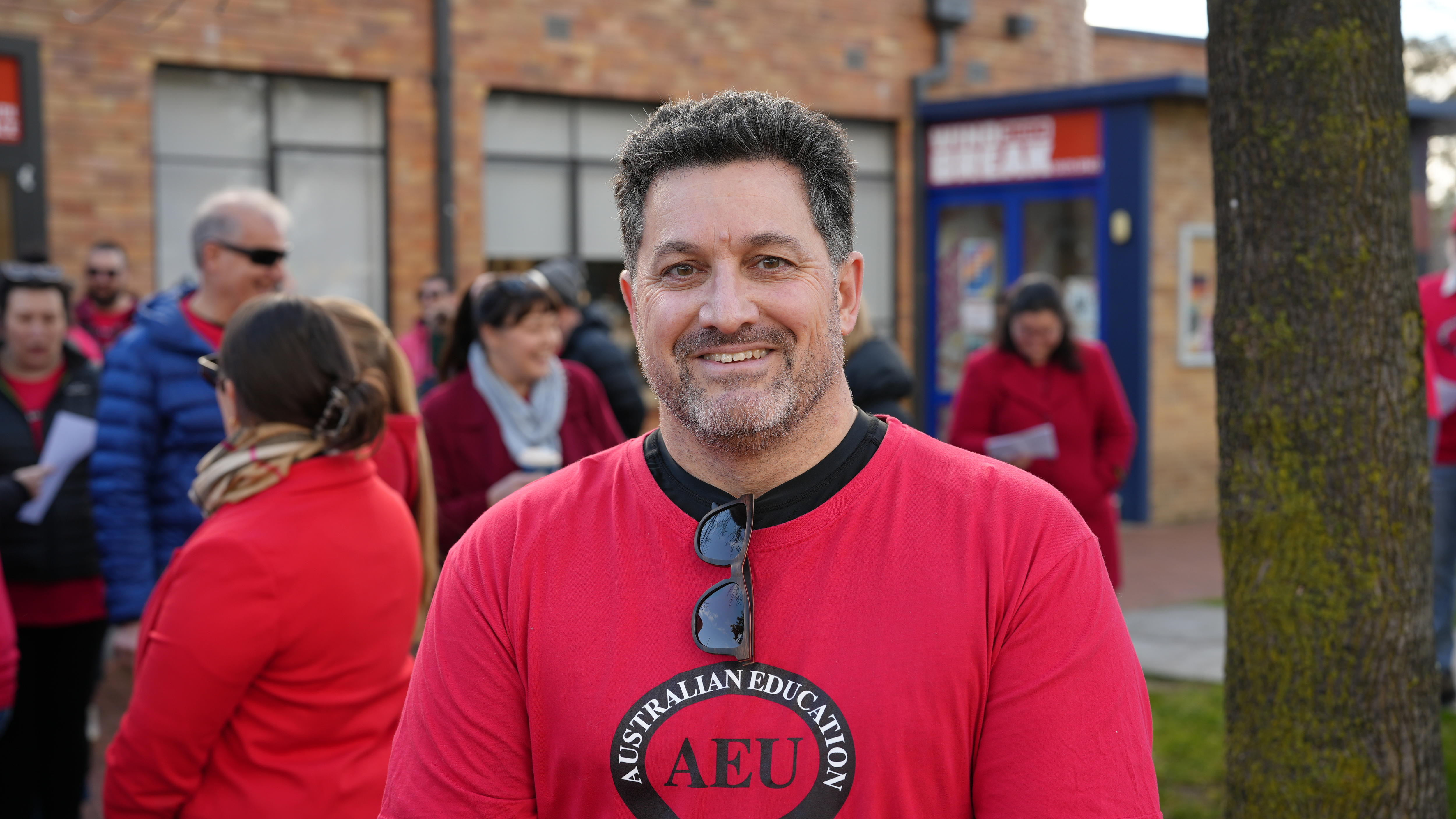A man wearing a red shirt and glasses hanging from his neckline at a protest rally
