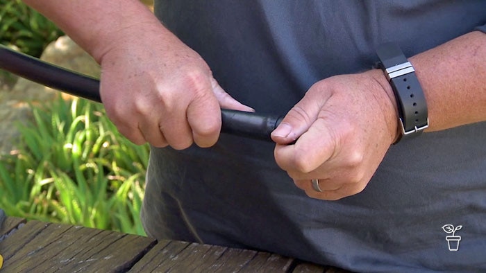 Hands pushing a fitting onto a piece of black plastic pipe