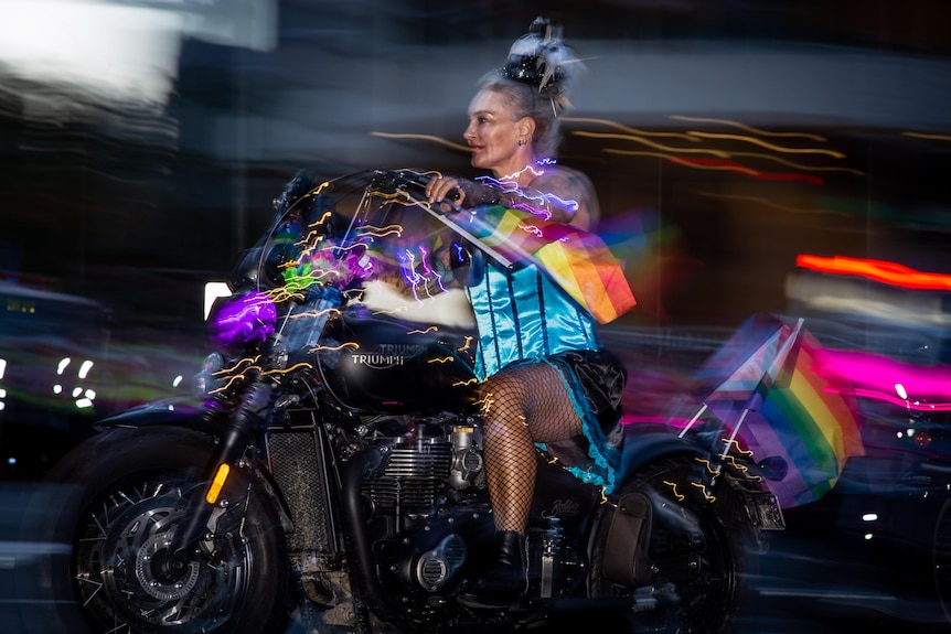 A woman without a helmet rides a motorcycle decorated with rainbow flags