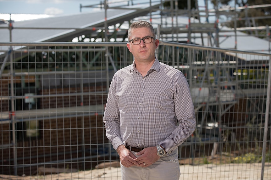 A man stands in front of a fence.