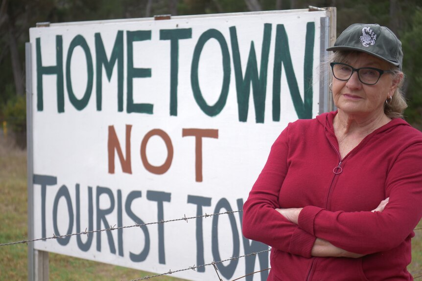 A woman with her arms crossed, standing in front of sign