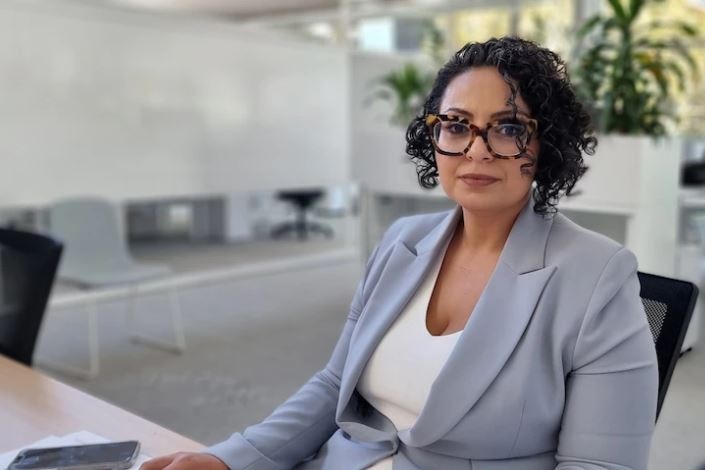 a woman wearing glasses looking at the camera while sitting at a desk in a boardroom