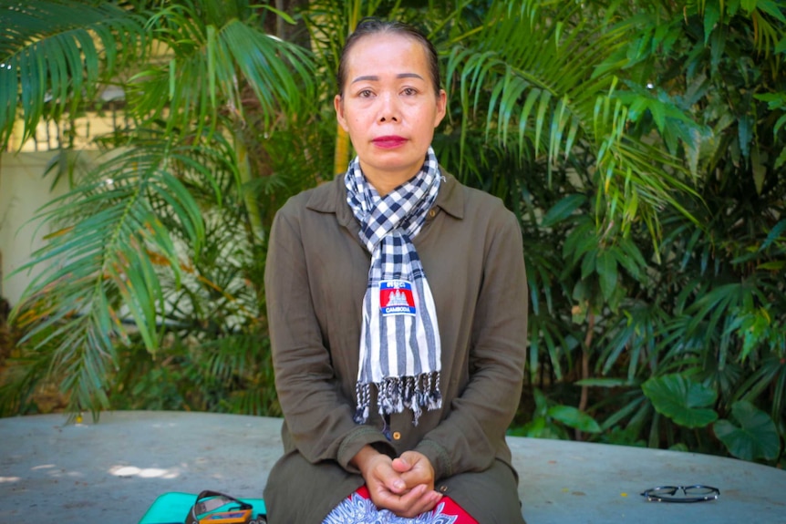 A woman sits in front of a tropical garden wearing a Cambodian scarf