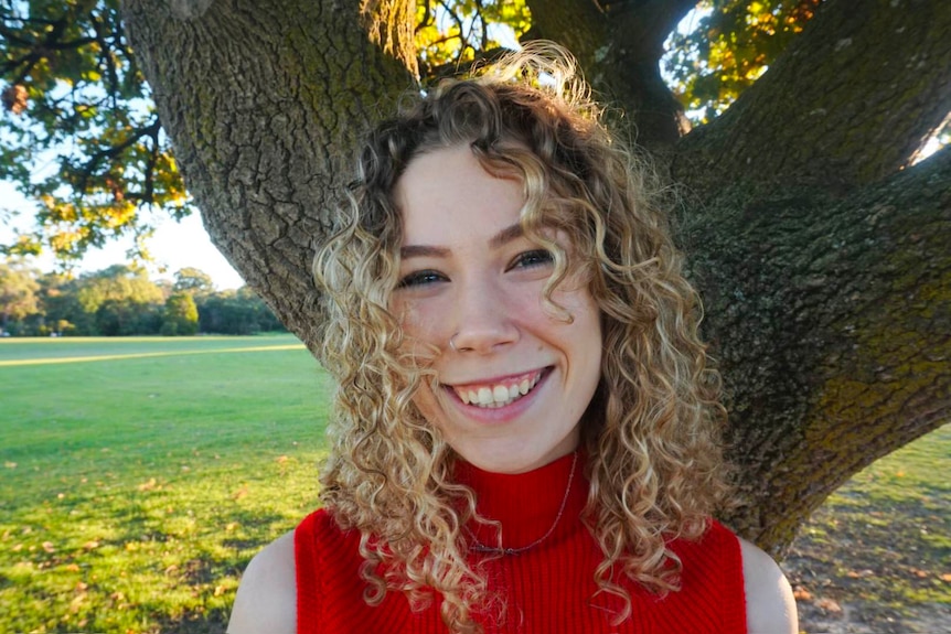 A woman with curly hair smiles for a photo in the park.