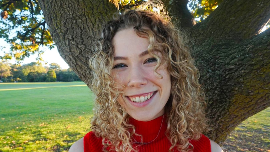 A woman with curly hair smiles for a photo in the park.