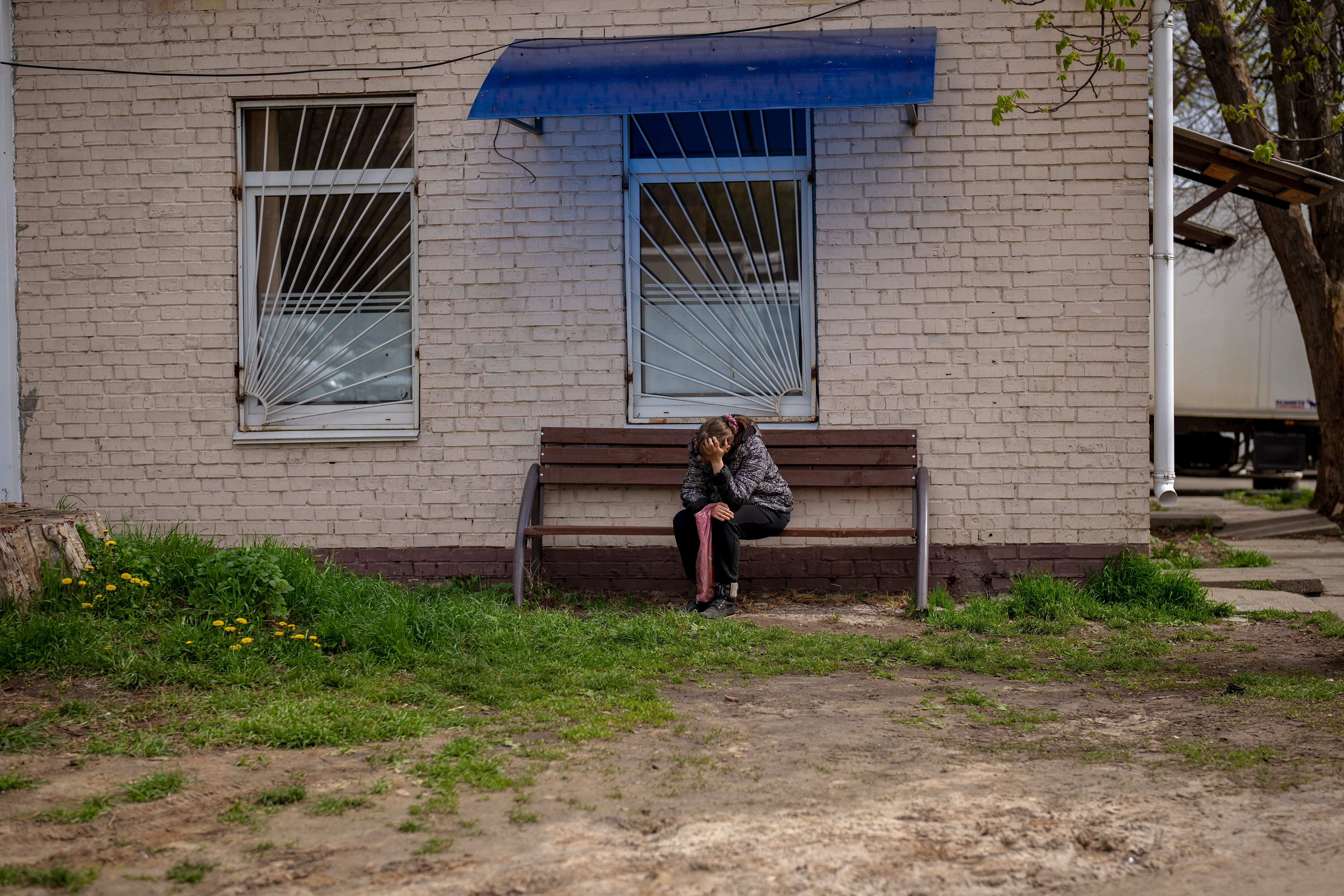 A woman sits on a bench, holding her head in her hands. 