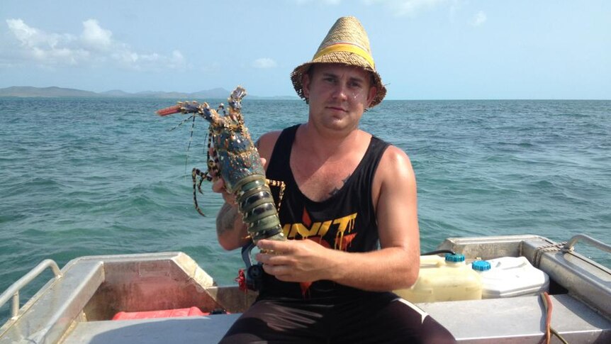 Man wearing straw hat and black singlet holding crayfish on stern of boat
