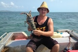 Man wearing straw hat and black singlet holding crayfish on stern of boat