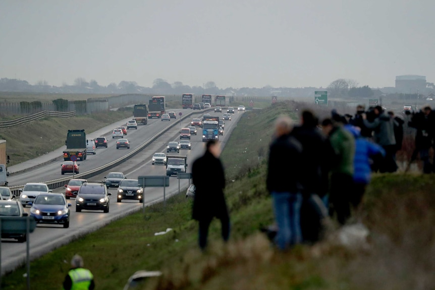People stand on a hill overlooking a line of trucks in the UK.