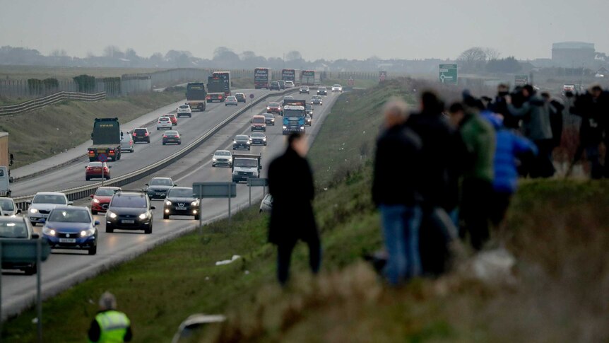 People stand on a hill overlooking a line of trucks in the UK.