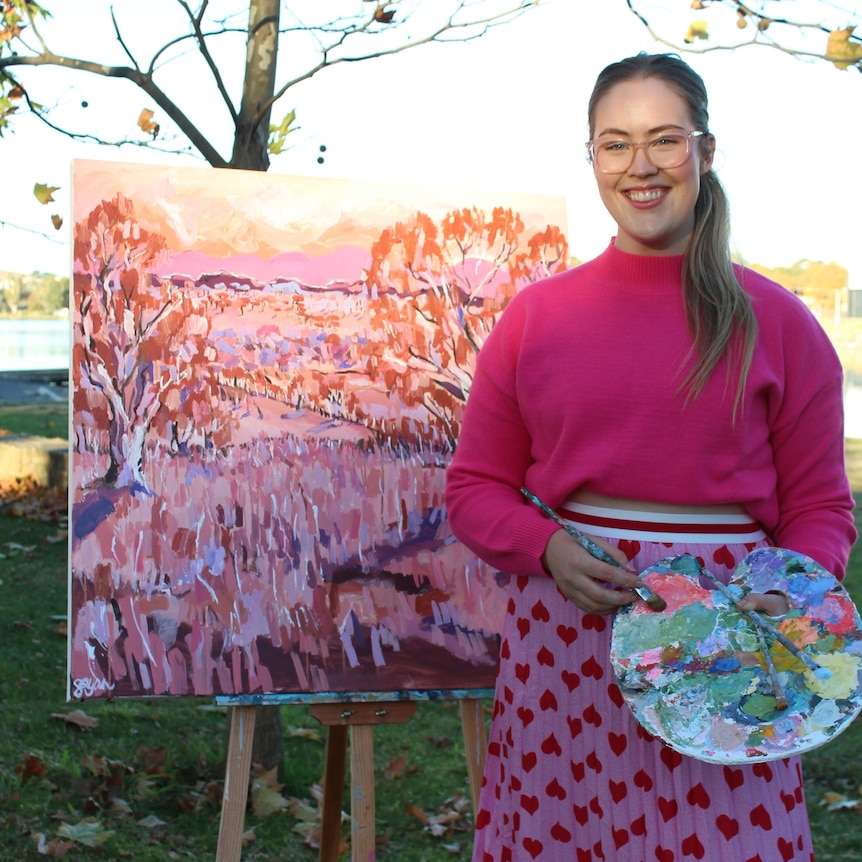 Artist Sophie Ryan stands beside her painting on canvas