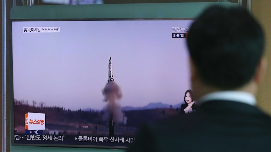 The back of a man's head as he watches a rocket launch on TV.