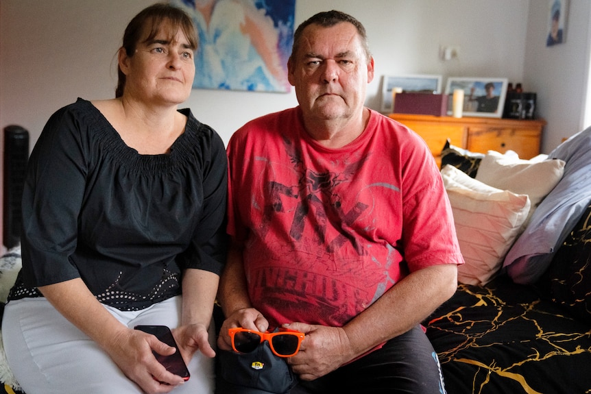 A middle-aged married couple sits sadly in a teenager's bedroom.
