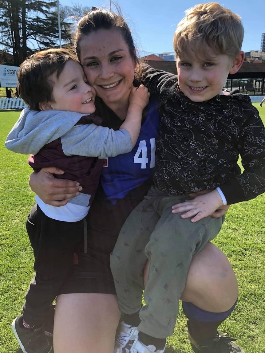 Jacara Egan is hugging her two young boys at a local footy field. They're all smiling. 