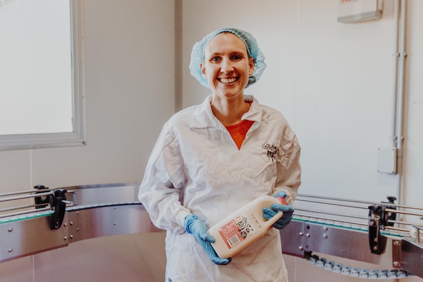 a woman dressed in ppe holds a bottle of milk