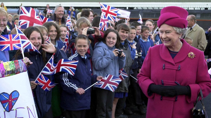 Queen Elizabeth smiles at a crowd of children holding Union Jack flags.