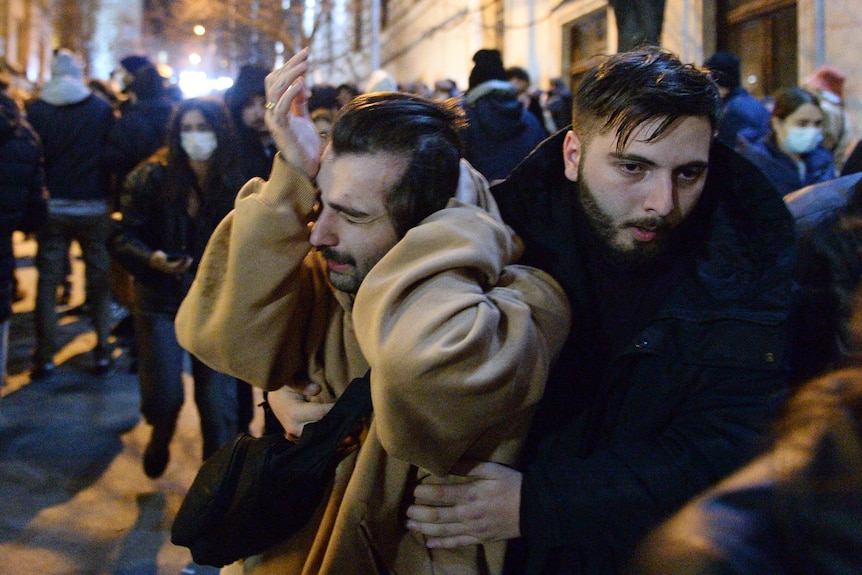 A man in clear agony is held up by a friend in the throes of a protest crowd