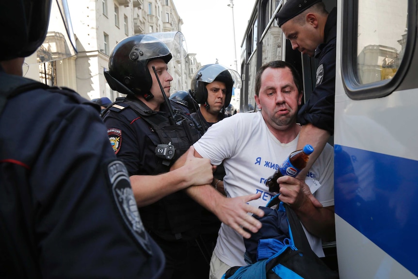 Police officers detain a man, dragging him into a police van.