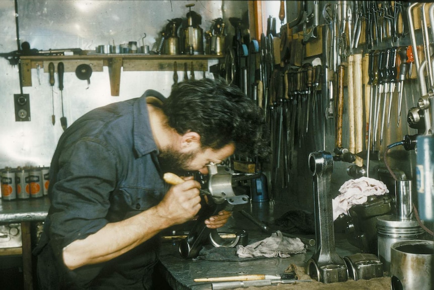 A man stands at a work bench covered in equipment from the 1950s.