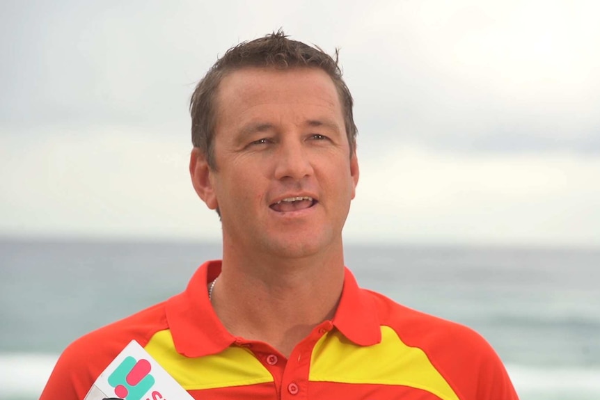 A man wearing a red and yellow polo shirt talks to members of the media.