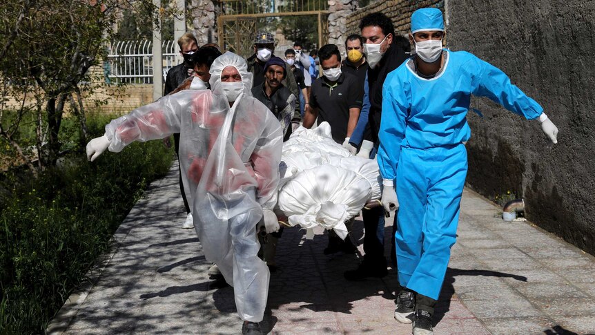 People in protective gear race a body wrapped in a sheet out of a Tehran apartment