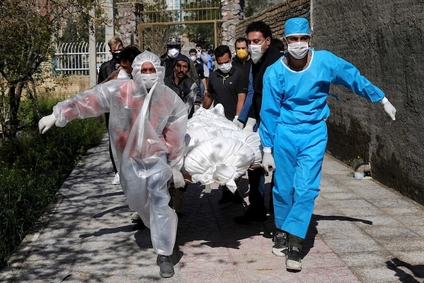 People in protective gear race a body wrapped in a sheet out of a Tehran apartment