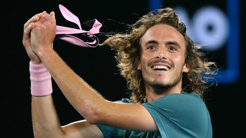 Stefanos Tsitsipas rips off his headband with a smile on his face.