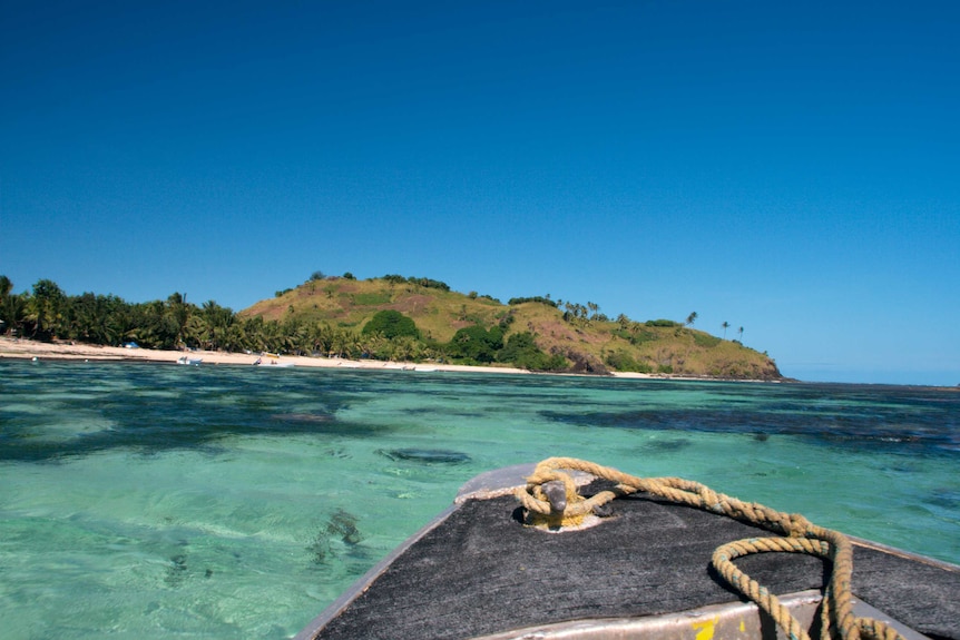 The bow of a boat can be seen travelling toward an island in Fiji.