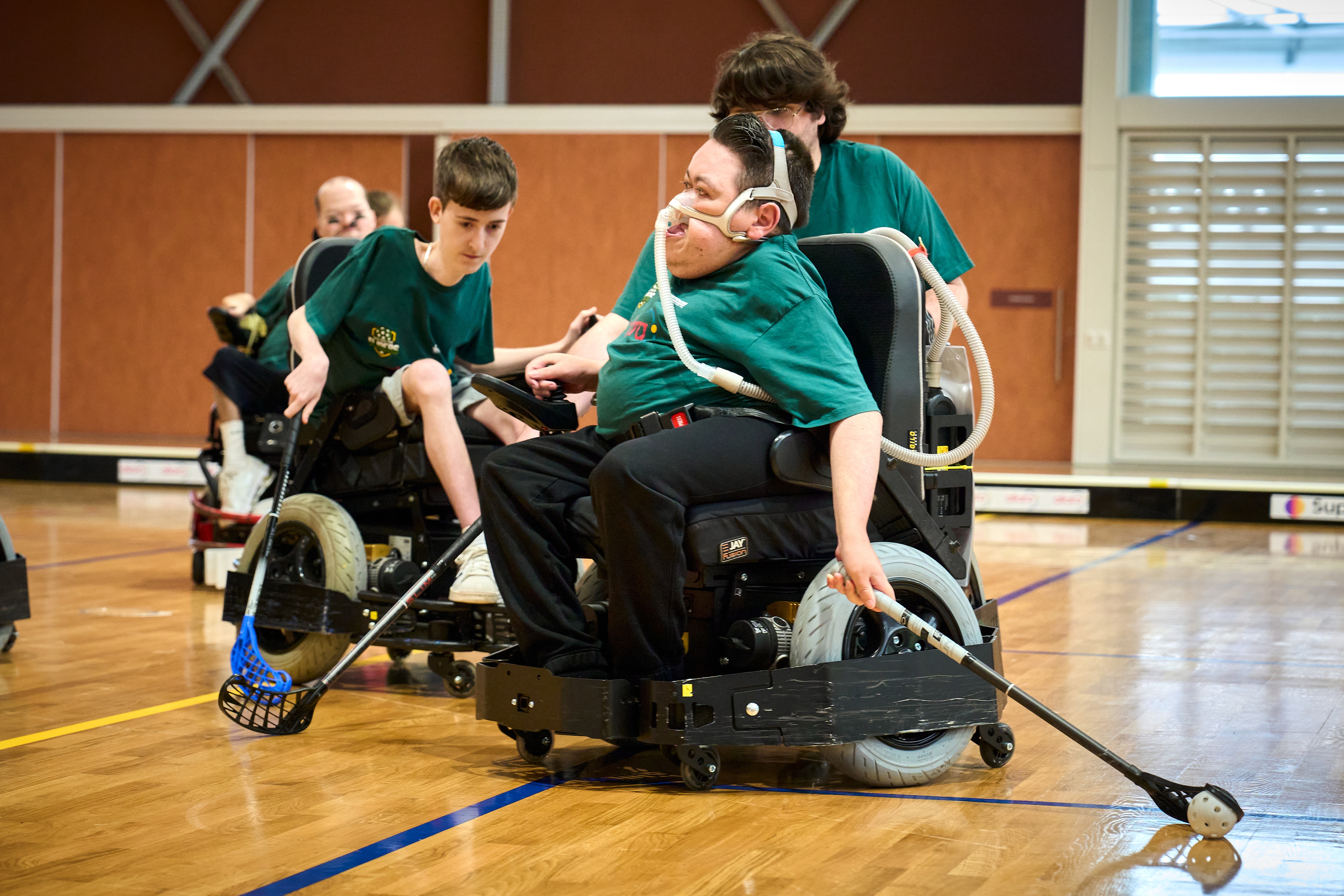 Jogadores em cadeiras de rodas motorizadas na quadra com tacos de hóquei