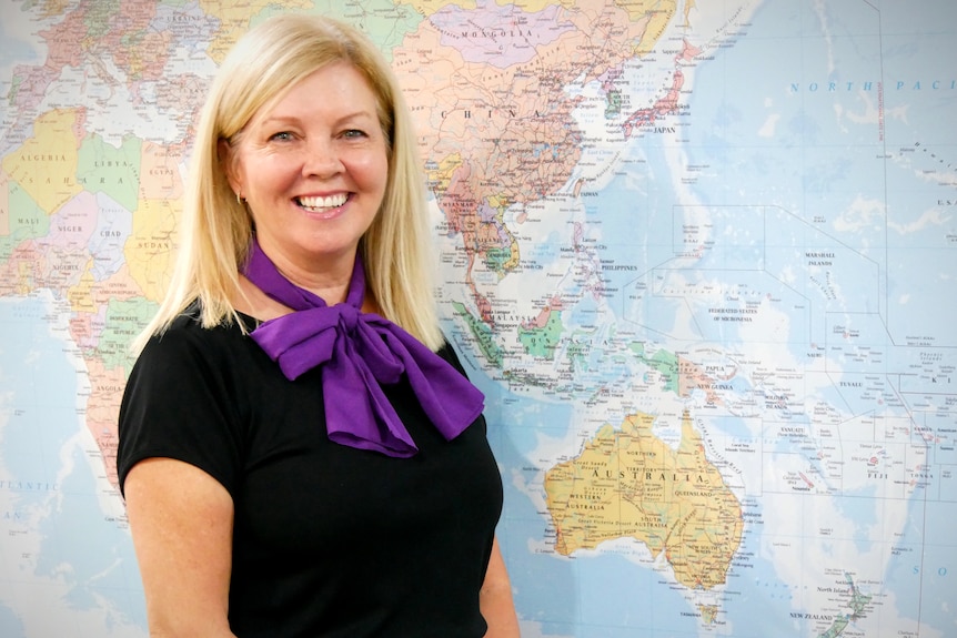 A woman smiles in front of a large map of the world