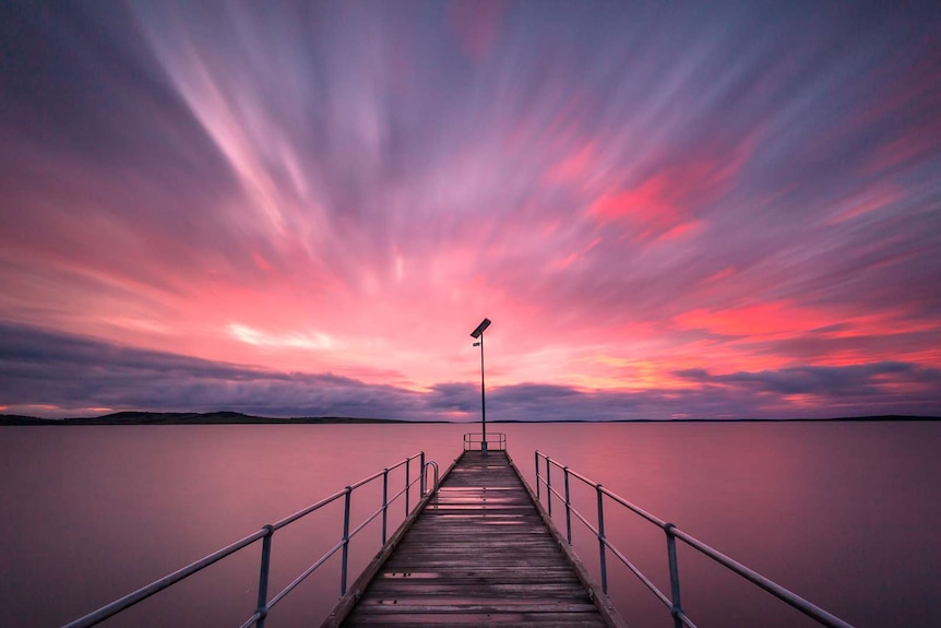 A pink and orange sunrise over a jetty jutting out into the sea