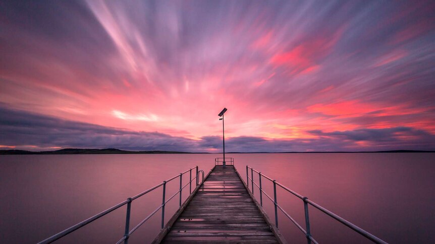 A pink and orange sunrise over a jetty jutting out into the sea