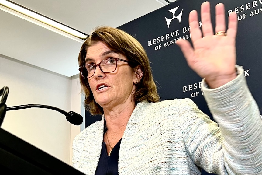 RBA governor Michele Bullock holds her hand up while speaking at a press conference.