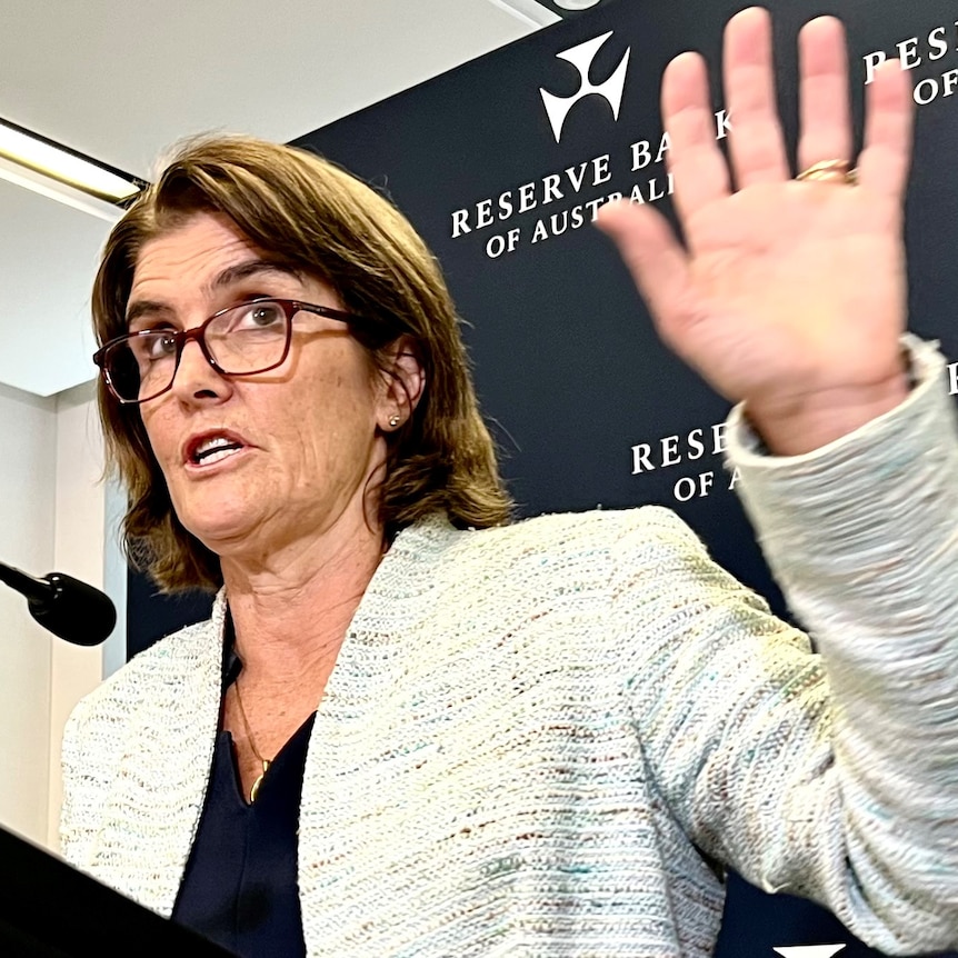 RBA governor Michele Bullock holds her hand up while speaking at a press conference.