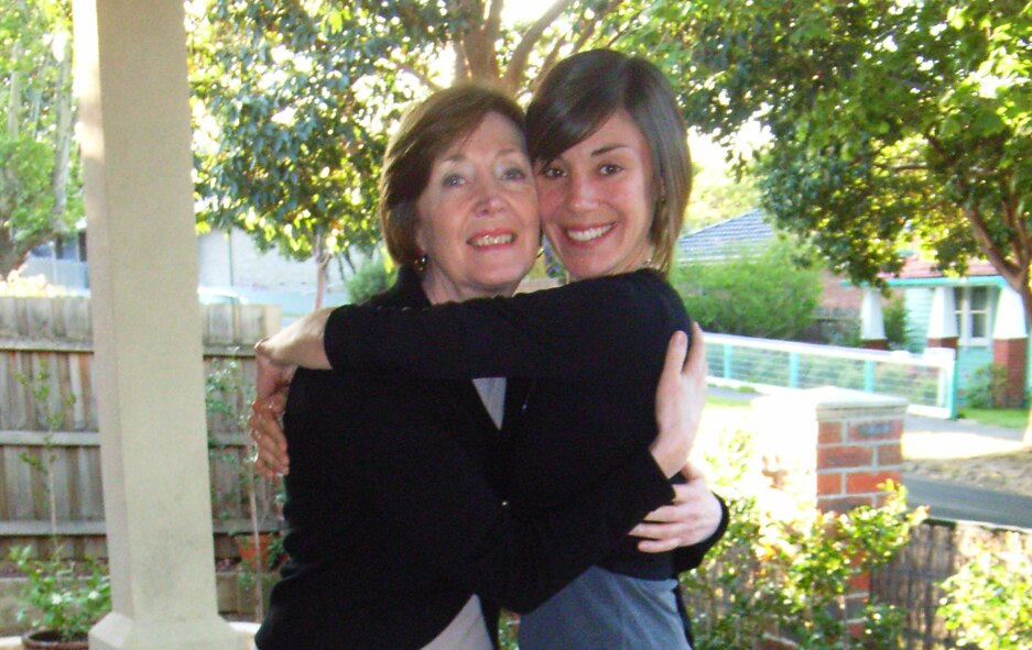 A woman hugs her adult daughter tight. The pair are smiling, standing outside 