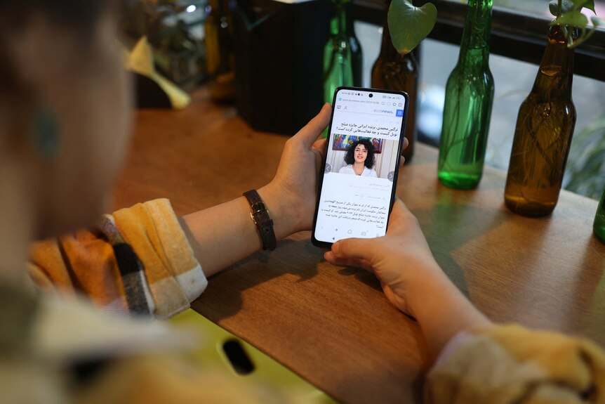 A person holds a smartphone with a news story about Narges Mohammadi 