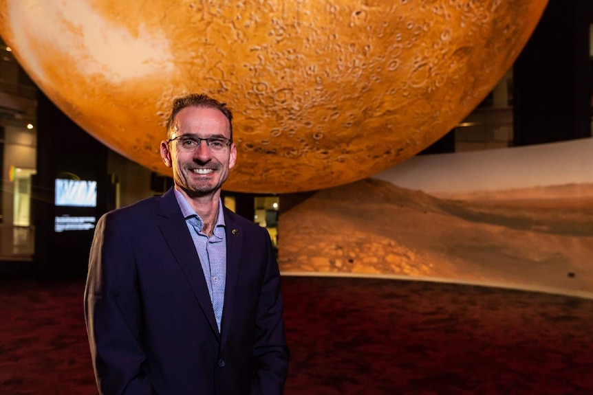 A photo of Anthony Murfett standing in front of a large model of Mars.