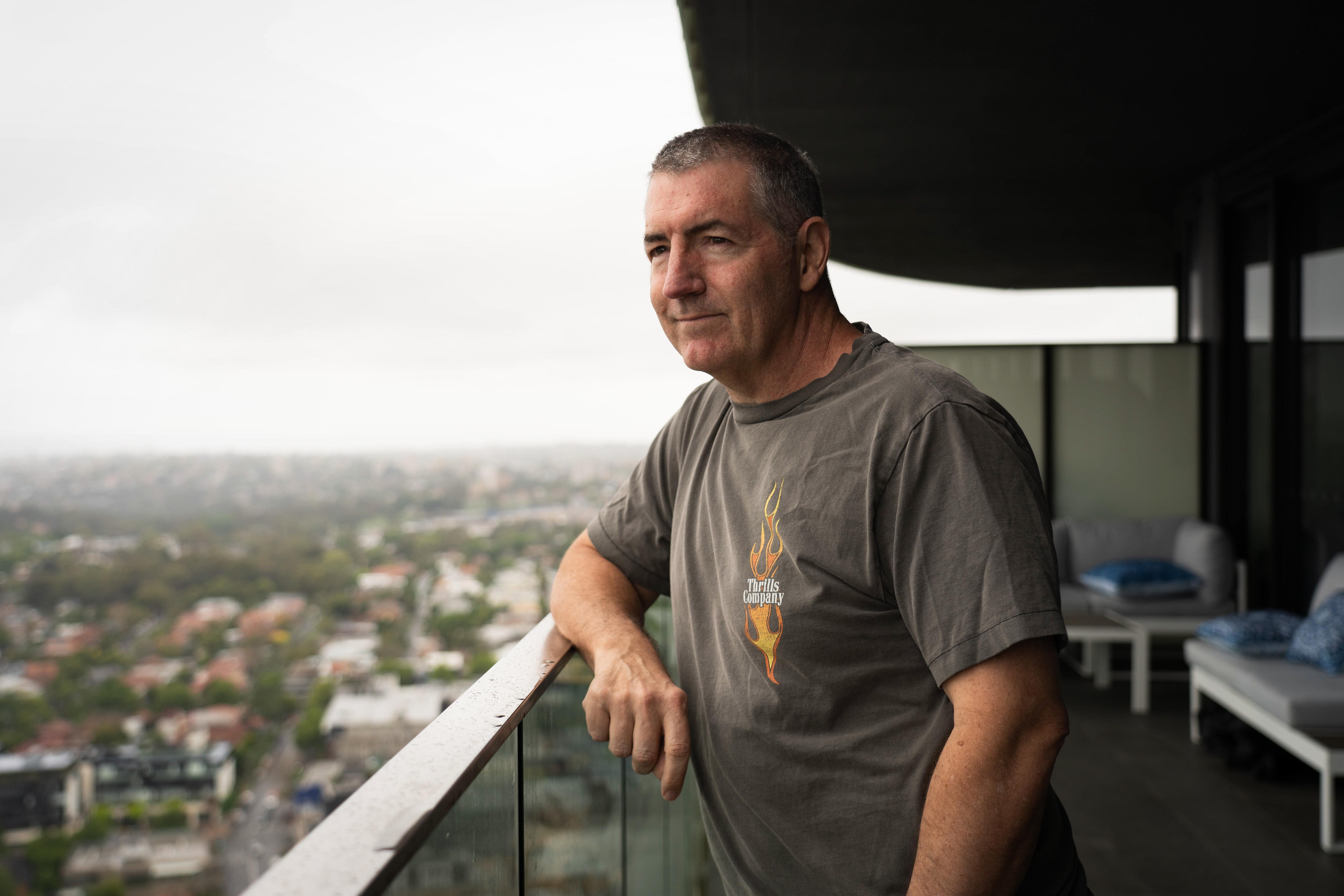 A man stands on a balcony of an apartment that looks over a suburban area.