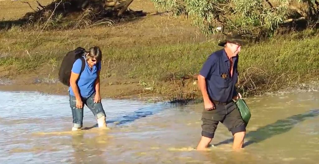 A woman and a man wade through knee-deep floodwaters near Winton.