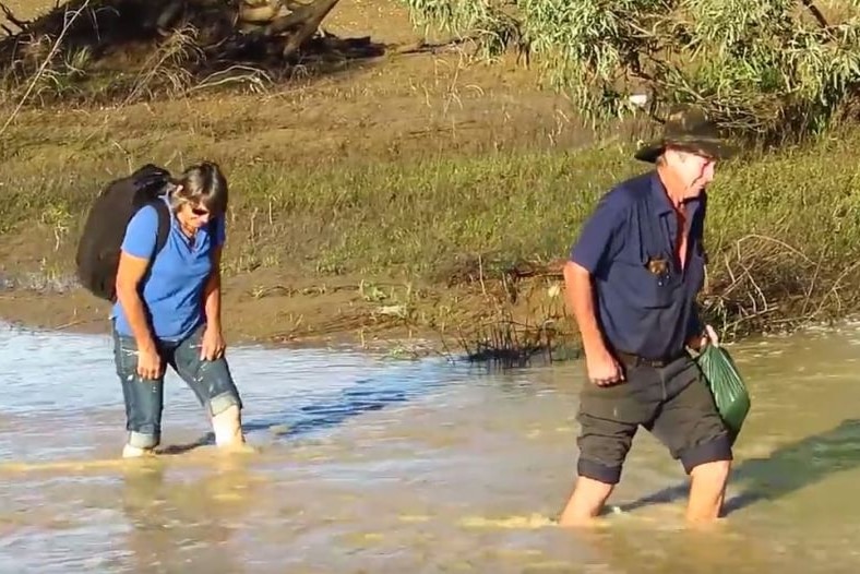 A woman and a man wade through knee-deep floodwaters near Winton.