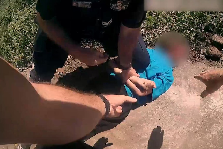 A police officer kneels on a face-down young person as they are arrested