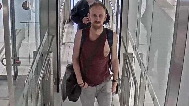 A CCTV image of a man in his 40s, wearing a maroon singlet and walking through a turnstile.