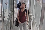 A CCTV image of a man in his 40s, wearing a maroon singlet and walking through a turnstile.