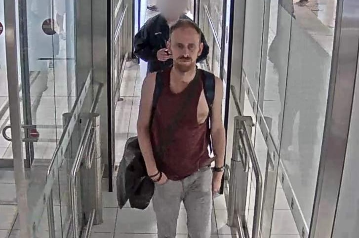 A CCTV image of a man in his 40s, wearing a maroon singlet and walking through a turnstile.