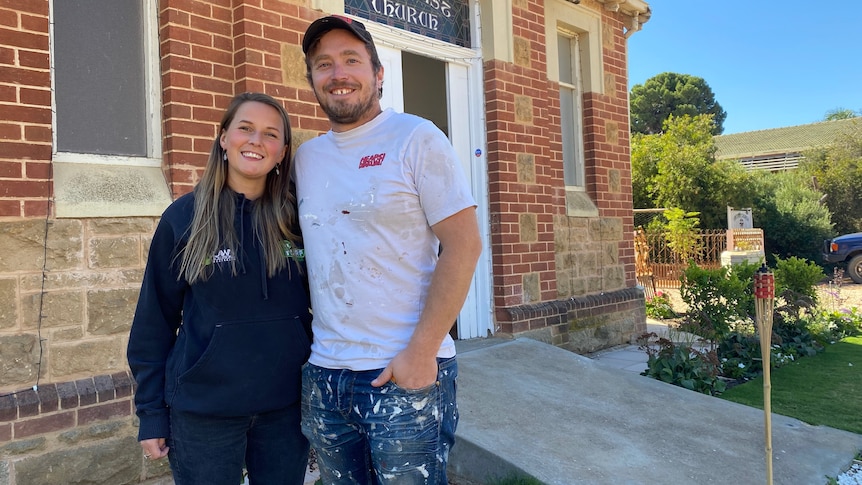 A woman and a man stand out the front of an old church building. 