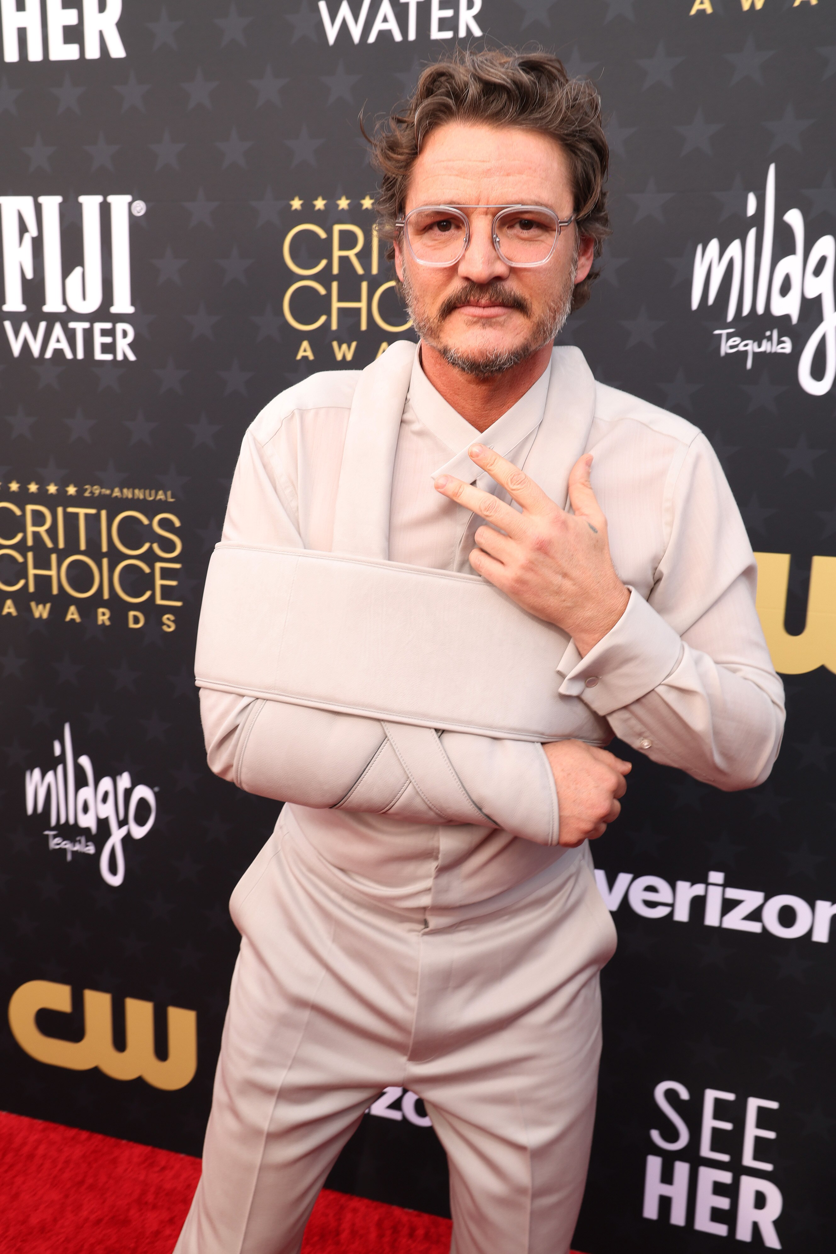 Pedro Pascal wearing a soft silky shirt, trousers and arm sling all in the exact same off-white tone